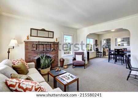 Simple room with brick fireplace and beige carpet floor. Dining room with black table set. Old house interior