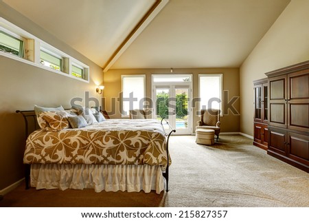 Luxury bedroom interior in soft beige color with beautiful bed, wardrobe. Room with high vaulted ceiling and walkout deck