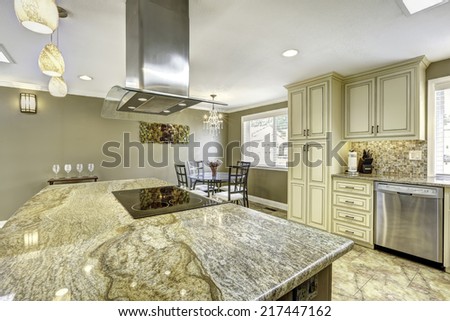 Spacious kitchen room with tile floor. Big kitchen island with built-in stove, granite top and steel hood