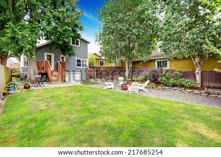 Small grey house with wooden walkout deck and patio area