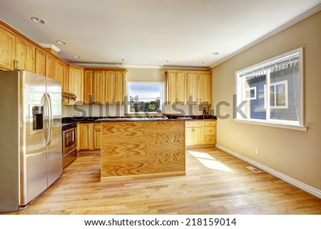 Kitchen room interior in empty house. Light brown wooden cabinets with black granite tops and steel refrigerator