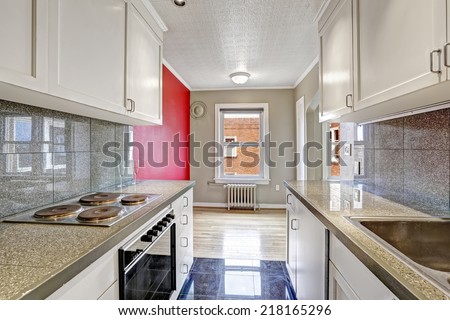 White kitchen cabinets with grey tile wall trim and tile floor. Empty dining area with grey and red walls