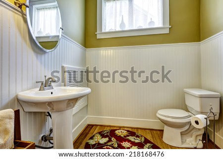Old bathroom interior with green wall and white plank panel trim. White toilet and washbasin stand