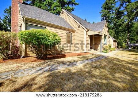 Simple house exterior. Front yard with dry grass and concrete tile walkway