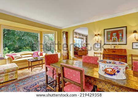 Bright yellow dining room with antique carved wood table and sitting area with wide window
