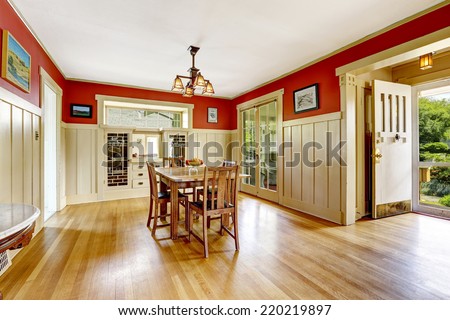 Dining room in old house with red and white wall trim. Furnished with old wooden table set. Room has exit to backyard area