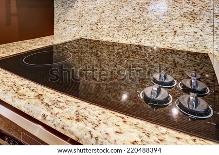 Modern built-in stove with shiny black flat surface. Granite counter top.