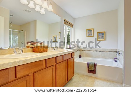 Bathroom with honey tone vanity cabinet and large mirror. Cabinet decorated with wicker basket for towels