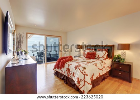 Romantic master bedroom interior with walkout deck. Bed with white and red bedding, decorated with pillows