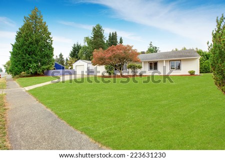 Simple house exterior in white color. Large front yard with lawn and trees