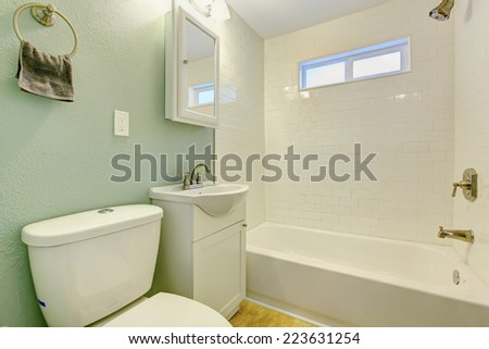 Mint bathroom interior with white tile wall trim, white bath tub, washbasin cabinet and toilet