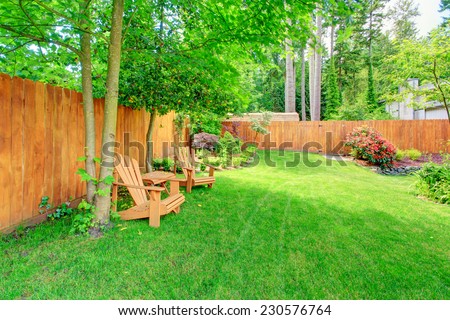 Fenced backyard with green lawn, flower beds and romantic sitting area with wooden chairs and table