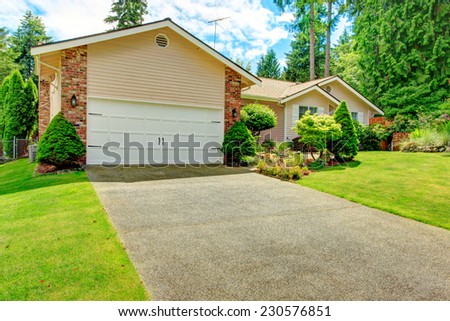 House exterior with garage and driveway. Beautiful flont yard landscape with lawn and decorative trees
