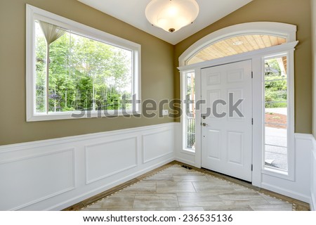 Entrance hallway with tile floor and beige wall with white trim. White door with arch and windows