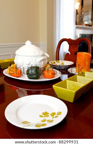 Dining room table setting for fall thanksgiving dinner. Orange and green colors and white plates in wood table.