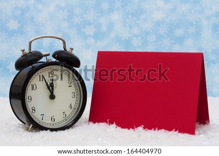 An old-fashion alarm clock with a blank red card on snow and a blue snowflake background, It is Christmas Time