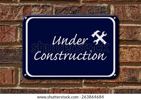 Under Construction Sign,  A blue sign with the words Under Construction with hammer and wrench on a brick wall