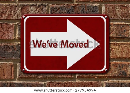 We have Moved Sign,  A red sign with the word We\'ve Moved with an arrow on a brick wall