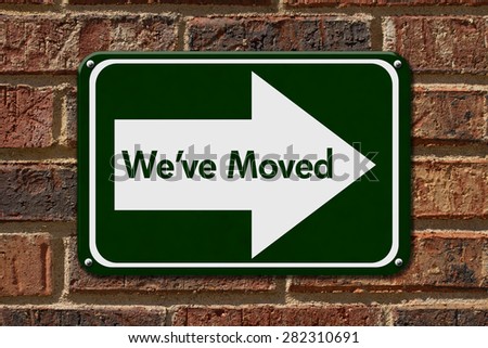 We have Moved Sign,  A green sign with the word We\'ve Moved with an arrow on a brick wall