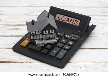 Calculating your mortgage payment, A gray model house on a calculator with word Loans over a distressed wood background