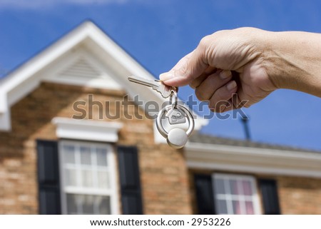 Woman holding a key for a house on a keychain in front of a brick house