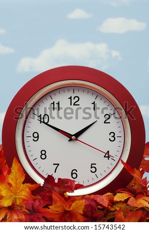 Red clock on fall leaves - the fall time change