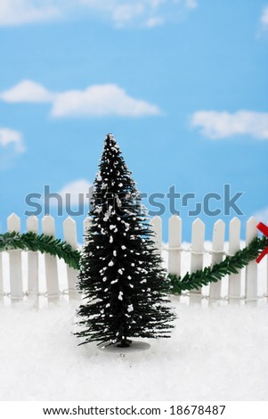 Evergreen tree and white picket fence with green garland and red bow, merry Christmas