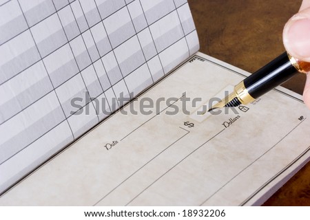 Hand holding pen writing in chequebook sitting on table, paying the bills