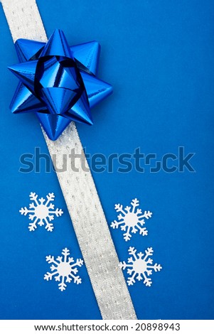 White ribbon and blue bow with snowflake on blue background making a present