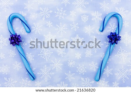Blue candy canes with bow sitting on a blue snowflake background, candy canes