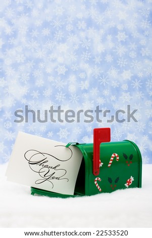 Green mailbox with white thank you card and the flag up sitting on snow with a snowflake background, mailbox