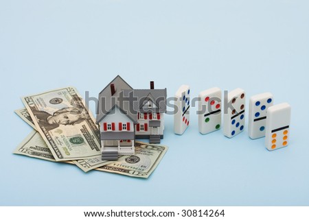 A model house with fallen dominoes sitting on a blue background, housing market