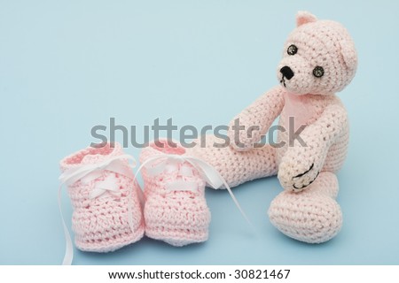 A pink handmade teddy bear and baby booties on a blue background, pink baby booties