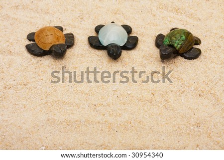 Three brown turtles with colourful shells sitting on a sand background, three turtles