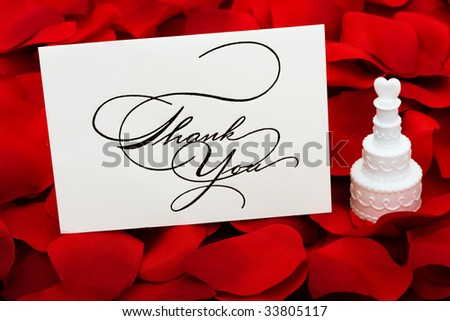 A white cakes with a heart on top and thank you card sitting on a red rose petal background, love cakes