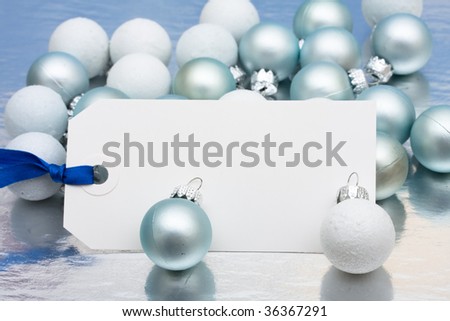 A blank Christmas gift tag sitting with glass balls on a shiny background, happy holidays present