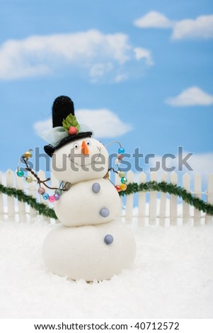 A snowman on a white picket fence with garland on a  sky background