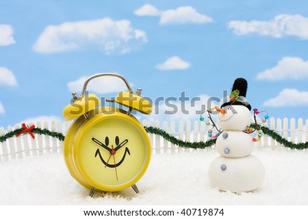 A yellow smiley face clock on a white picket fence with garland on a  sky background, winter time