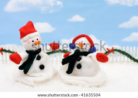 Two snowmen on a white picket fence with garland on a  sky background, gingerbread house