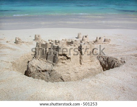 A sandcastle stands at the water\'s edge on a Hawaiian beach as gentle waves lap the shore.