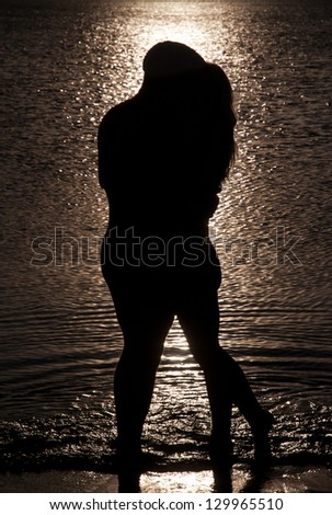 Young couple hug silhouette on a sea beach against sunset background