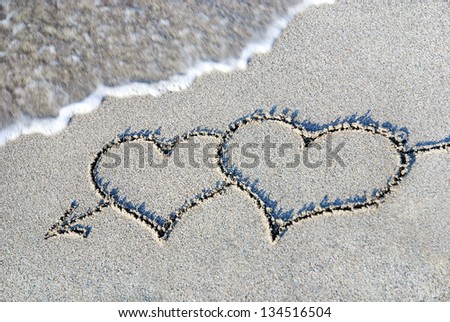 two hearts outline with arrow on the wet brilliance beach sand against wave