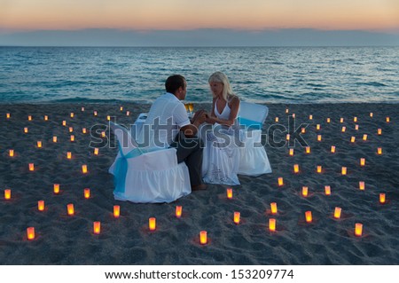 lovers couple share a romantic dinner with candles on sandy sea beach during sunset