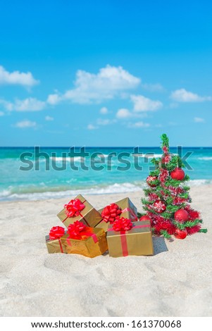 Christmas tree and golden gift with big red bow on the sea sandy beach. Christmas vacation concept.