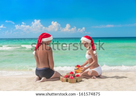 Man in red santa hat  giving a present to his blonde girlfriend on the sea beach - christmas vacations concept