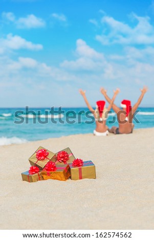 happy couple in santa hats hands up at sea beach with christmas packed  golden gifts