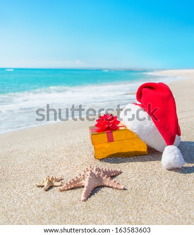 Santa Claus hat and gold christmas gift box on the seashore with sea stars against blue sky