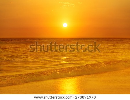 Bright fiery sunset above wavy sea surface with golden sun path and sand - nature background