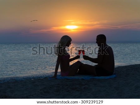 Loving couple drinking red wine at summer sandy sea beach during sunset time