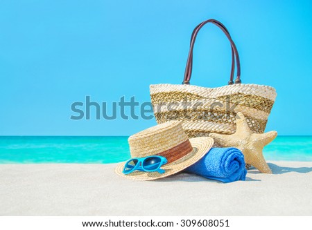Closeup of summer straw bag, hat, towel and sunglasses on sandy beach with sea-star - summertime vacation concept